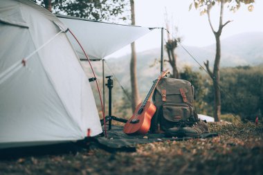 Kamp malzemeleri, çantalar, ayakkabılar, ukulele, sabahları çadırın yanında tripod. Nesne kampı, seyahat ve meslek kavramı.