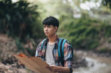 Sırt çantalı bir yürüyüşçü ormanda nehrin yanında yol tarifi bulmak için haritasını çıkarmış. yürüyüş ve macera konsepti.