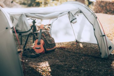 Kamp malzemeleri, çantalar, ayakkabılar, ukulele, sabahları çadırda tripod. Nesne kampı, seyahat ve meslek kavramı.