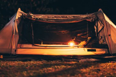 Geceleri çadırın zemininde bir gaz lambası ve yanında ukulele ve ayakkabı olan bir çanta var. Kamp malzemeleri, meslek ve seyahat konsepti.