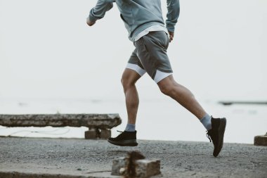 Sahil kenarındaki eski köprüde koşan sağlıklı yaşam tarzı genç bir fitness adamı. Açık hava sporu, sağlıklı yaşam tarzı konsepti.