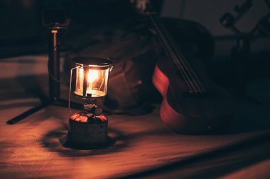 Geceleri çadırın zemininde bir gaz lambası ve yanında ukulele ve ayakkabı olan bir çanta var. Kamp malzemeleri, meslek ve seyahat konsepti.