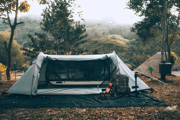 stock image Gray tent on the grass in the forest The view behind is the mountain in the morning. Camping, Travel and holiday concept.