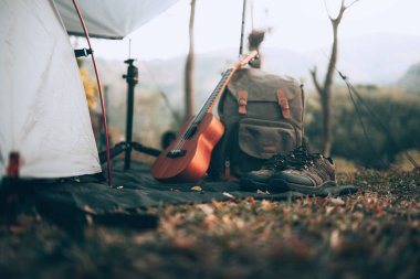 Kamp malzemeleri, çantalar, ayakkabılar, ukulele, sabahları çadırın yanında tripod. Nesne kampı, seyahat ve meslek kavramı.