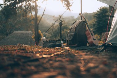 Kamp malzemeleri, çantalar, ayakkabılar, ukulele, sabahları çadırın yanında tripod. Nesne kampı, seyahat ve meslek kavramı.