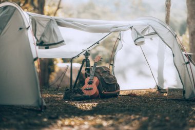 Kamp malzemeleri, çantalar, ayakkabılar, ukulele, sabahları çadırda tripod. Nesne kampı, seyahat ve meslek kavramı.