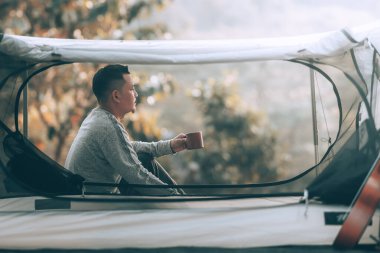 Tatilde ormanda kamp yaparken sabahları kahve içen bir adam. Meslek ve seyahat kavramı.