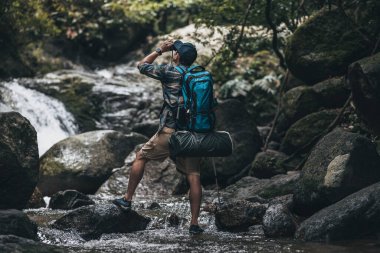 Kayaların üzerinde duran yürüyüşçüler hayvanları görmek için dürbün kullanırlar ve ormandaki sırt çantaları ve şelale arkaplanlı manzarayı görürler. yürüyüş ve macera konsepti.