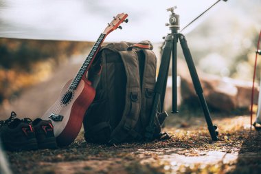 Kamp malzemeleri, çantalar, ayakkabılar, ukulele, sabahları çadırda tripod. Nesne kampı, seyahat ve meslek kavramı.