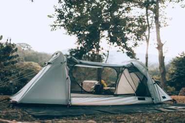 Ormandaki çimlerin üzerindeki gri çadır Arkadaki manzara sabahları dağdır. Kamp, seyahat ve tatil konsepti.