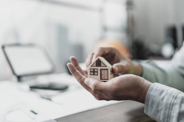 Mimar mühendis elleri taslak üzerinde mini ev modelini tutuyor ve koruyor. Evi sat, koru, maliyet planlama ve inşaat konsepti.