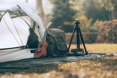 Kamp malzemeleri, çantalar, ayakkabılar, ukulele, sabahları çadırın yanında tripod. Nesne kampı, seyahat ve meslek kavramı.