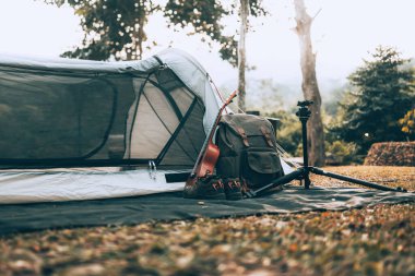 Kamp malzemeleri, çantalar, ayakkabılar, ukulele, sabahları çadırın yanında tripod. Nesne kampı, seyahat ve meslek kavramı.