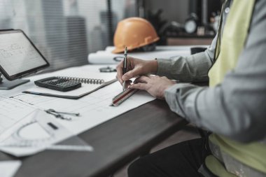 Engineering working with drawings inspection and writing on the office desk and Calculator, triangle ruler, safety glasses, compass, vernier caliper on Blueprint. Engineer, Architect, Industry and factory concept.