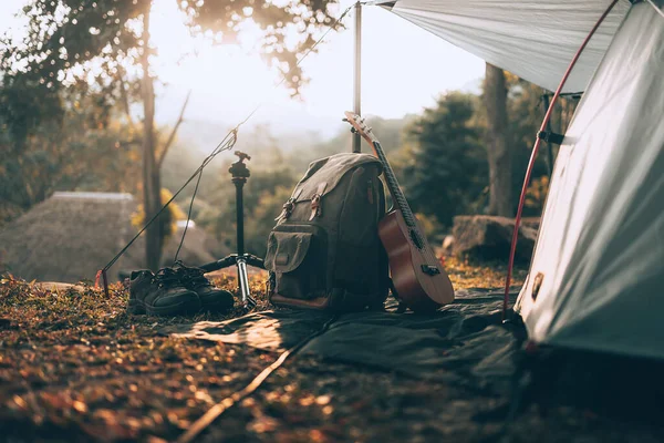 Kamp malzemeleri, çantalar, ayakkabılar, ukulele, sabahları çadırın yanında tripod. Nesne kampı, seyahat ve meslek kavramı.