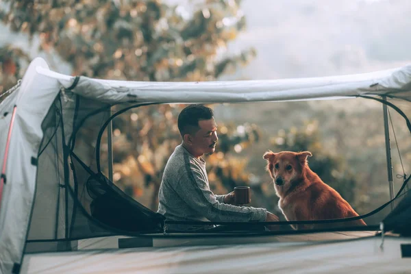 Man drink coffee and relax with dog in the morning during a camping trip in the forest on holiday. Vocation and travel concept.