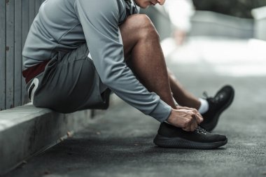 Kardiyo çalışmasından önce spor ayakkabılarına ayakkabı bağlayan bir adam şehir merkezindeki parkta koşuyor. Büyük şehir yaşam konseptinde sağlık ve yaşam tarzı.