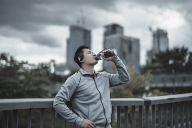 Genç sporcu adam koşudan sonra su içer, parkta koşar. Spor susuzluğu ve egzersizden sonra dinlenme. Büyük şehir yaşam konseptinde sağlık ve yaşam tarzı.