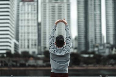 Kardiyo çalışmasından önce şehir merkezindeki parkta kaslarını çalıştıran bir adam. Büyük şehir yaşam konseptinde sağlık ve yaşam tarzı.