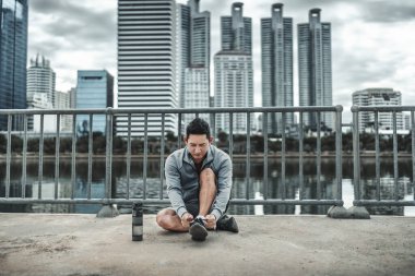 Kardiyo çalışmasından önce spor ayakkabılarına ayakkabı bağlayan bir adam şehir merkezindeki parkta koşuyor. Büyük şehir yaşam konseptinde sağlık ve yaşam tarzı.