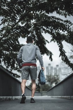 Kardiyo çalışmasından önce şehir merkezindeki parkta yaya köprüsünde yürüyen bir adam. Büyük şehir yaşam konseptinde sağlık ve yaşam tarzı.
