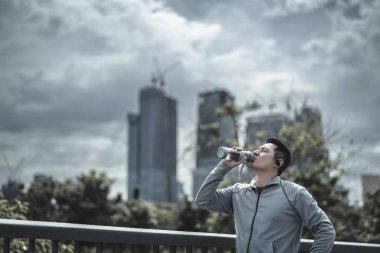 Genç sporcu adam koşudan sonra su içer, parkta koşar. Spor susuzluğu ve egzersizden sonra dinlenme. Büyük şehir yaşam konseptinde sağlık ve yaşam tarzı.