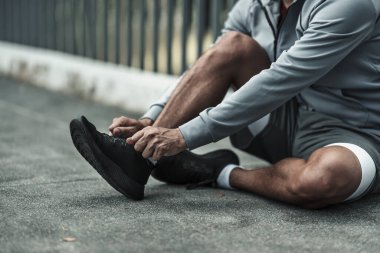 Kardiyo çalışmasından önce spor ayakkabılarına ayakkabı bağlayan bir adam şehir merkezindeki parkta koşuyor. Büyük şehir yaşam konseptinde sağlık ve yaşam tarzı.