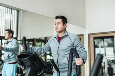 Spor salonunda eliptik antrenör kullanan bir adam. Spor, spor, spor ve sağlık konsepti.