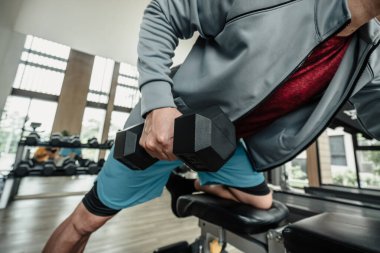 Spor salonunda dambılla triseps kası egzersizi yapan bir adam. Fitness, egzersiz ve trans konsepti.