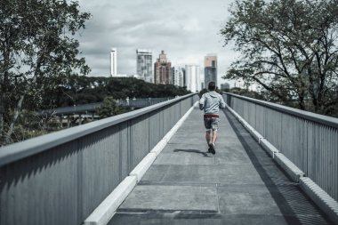 Kardiyo çalışması için şehir merkezindeki parkta yaya köprüsünde koşan bir adam. Büyük şehir yaşam konseptinde sağlık ve yaşam tarzı.