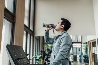 Spor salonunda koşu bandında su içen bir adam. Spor, spor, egzersiz ve yaşam tarzı konsepti.