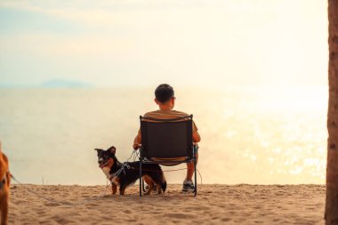 Köpek sahibi sahilde bir sandalyede oturuyor ve gün batımını seyrediyor.. 