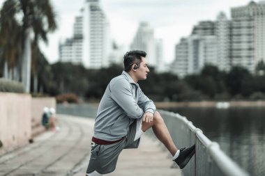 Kardiyo çalışmasından önce şehir merkezindeki parkta kaslarını çalıştıran bir adam. Büyük şehir yaşam konseptinde sağlık ve yaşam tarzı.