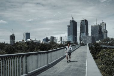 Kardiyo çalışması için şehir merkezindeki parkta yaya köprüsünde koşan bir adam. Büyük şehir yaşam konseptinde sağlık ve yaşam tarzı.