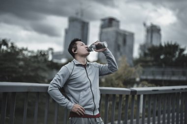 Genç sporcu adam koşudan sonra su içer, parkta koşar. Spor susuzluğu ve egzersizden sonra dinlenme. Büyük şehir yaşam konseptinde sağlık ve yaşam tarzı.