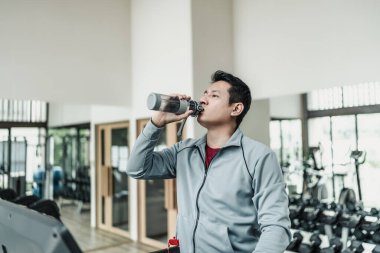 Spor salonunda koşu bandında su içen bir adam. Spor, spor, egzersiz ve yaşam tarzı konsepti.