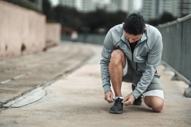 Kardiyo çalışmasından önce spor ayakkabılarına ayakkabı bağlayan bir adam şehir merkezindeki parkta koşuyor. Büyük şehir yaşam konseptinde sağlık ve yaşam tarzı.
