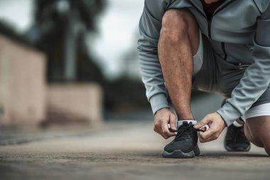 Kardiyo çalışmasından önce spor ayakkabılarına ayakkabı bağlayan bir adam şehir merkezindeki parkta koşuyor. Büyük şehir yaşam konseptinde sağlık ve yaşam tarzı.
