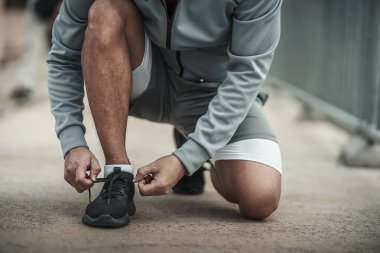 Kardiyo çalışmasından önce spor ayakkabılarına ayakkabı bağlayan bir adam şehir merkezindeki parkta koşuyor. Büyük şehir yaşam konseptinde sağlık ve yaşam tarzı.