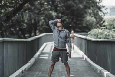 Yorgun bir genç adam terini siliyor. Adam dinleniyor, nefes alıyor ve parkta bir şişe içme suyu tutuyor. Büyük şehir yaşam konseptinde sağlık ve yaşam tarzı.