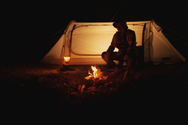 Yürüyüşçüler çadırın önünde şenlik ateşi yakar. Kamp ateşi, kamp kavramı.