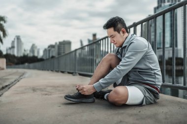 Kardiyo çalışmasından önce spor ayakkabılarına ayakkabı bağlayan bir adam şehir merkezindeki parkta koşuyor. Büyük şehir yaşam konseptinde sağlık ve yaşam tarzı.