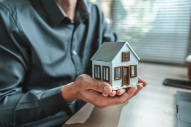 Ev satış elemanı, sigorta satıcısı elinde bir ev tutuyor. Varlıklar, gayrimenkul, krediler ve gayrimenkul kavramı.