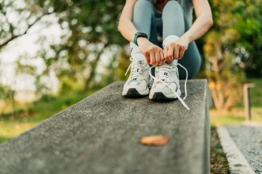 Spor kıyafetleri giymiş bir kadın ayakkabı bağcıklarını bağlıyor, koşmaya ve parkta egzersiz yapmaya hazırlanıyor..