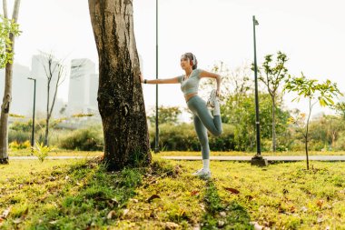 Spor kıyafetleri giymiş bir kadın kulaklık takıyor ve egzersiz yapmadan önce, koşmadan önce ya da egzersizden sonra kaslarını esnetirken müzik dinliyor..