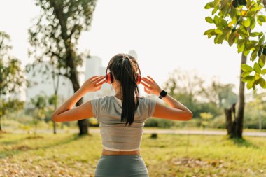 Spor kıyafetleri giymiş bir kadın kulaklık takıyor ve egzersiz yapmadan önce, koşmadan önce ya da egzersizden sonra kaslarını esnetirken müzik dinliyor..