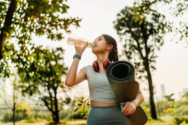 Spor kıyafetleri giymiş bir kadın egzersiz molasında su içiyor. Spor, egzersiz, egzersiz, yoga ve spor konsepti..
