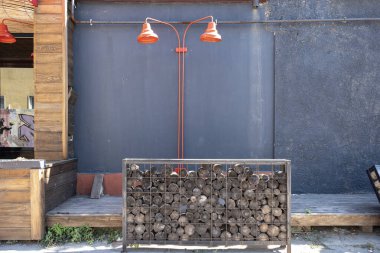 Caddedeki gri bir duvarda iki kırmızı abajur. Gri bir duvarın arkasındaki ahşap kutuda lamba..