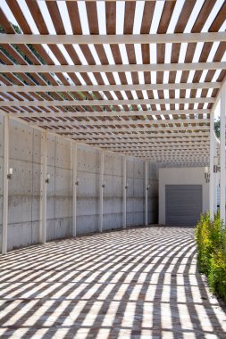 Bir yaz günü ahşap pergola gölgesinde modern bir binaya giden yol..