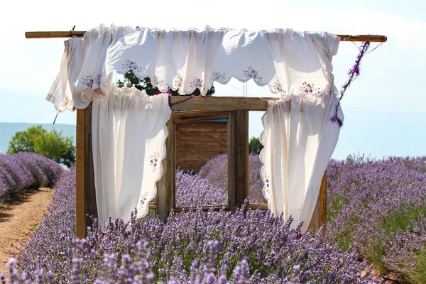 Decor with white curtains in a lavender field, wooden window scene. A view of a lavender field.